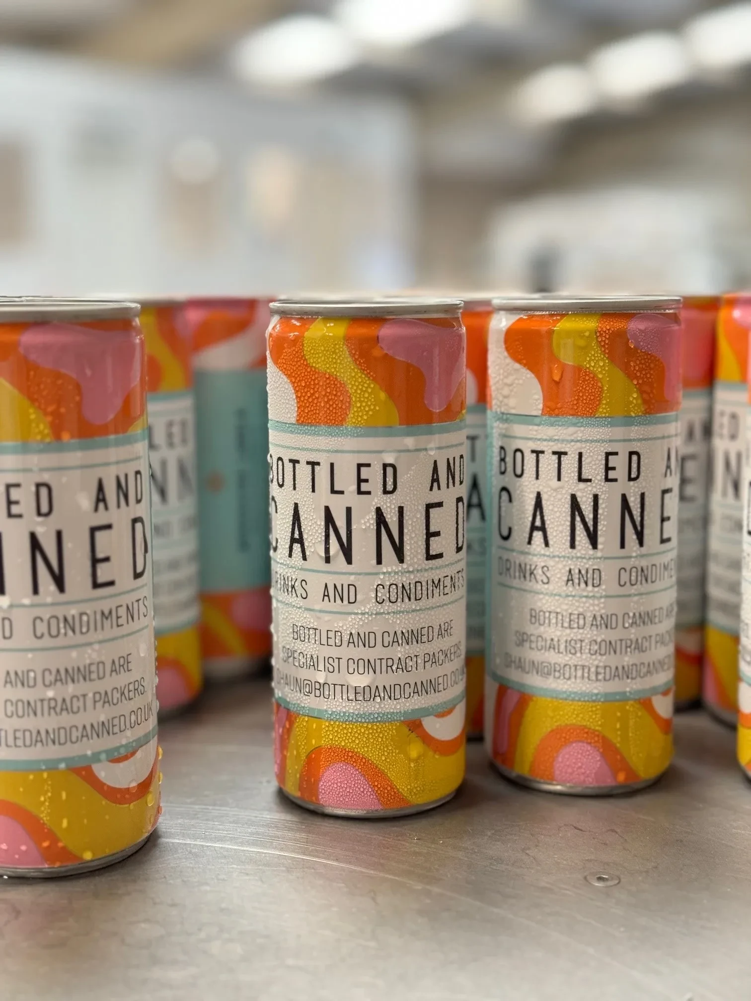 Cans with colorful orange, pink, and yellow swirl designs labeled 'Bottled and Canned Drinks and Condiments'.