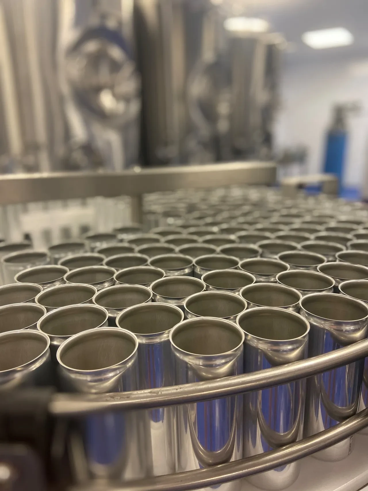 Close-up of empty shiny aluminum cans arranged in rows on a metal conveyor in a factory.